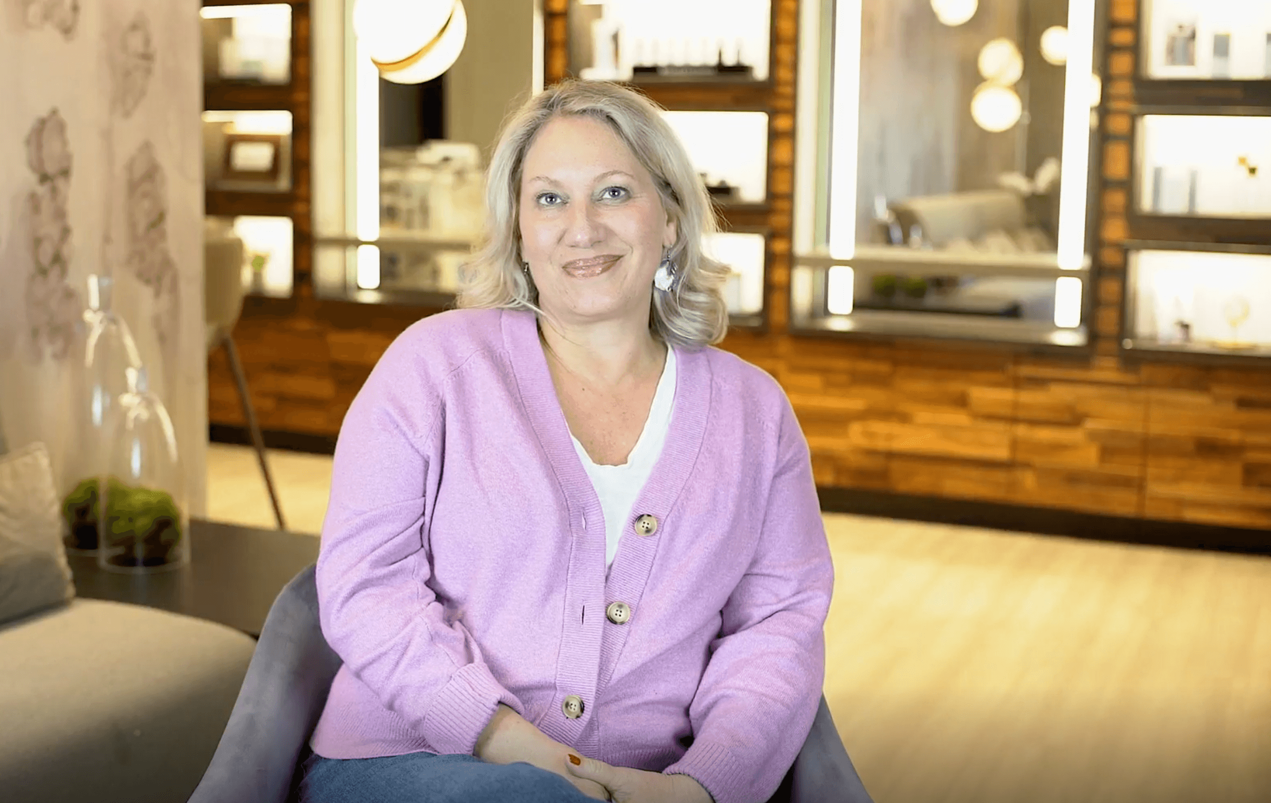 Blonde woman in purple sweater sitting in a chair smiling at the camera